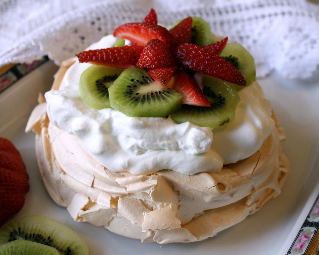 Sladká pusinka z bílkového sněhu použitá jako dortový korpus: naplněná šlehačkou či krémem a odzobená ovocem Sněhový dort Pavlova s jahodami a kiwi